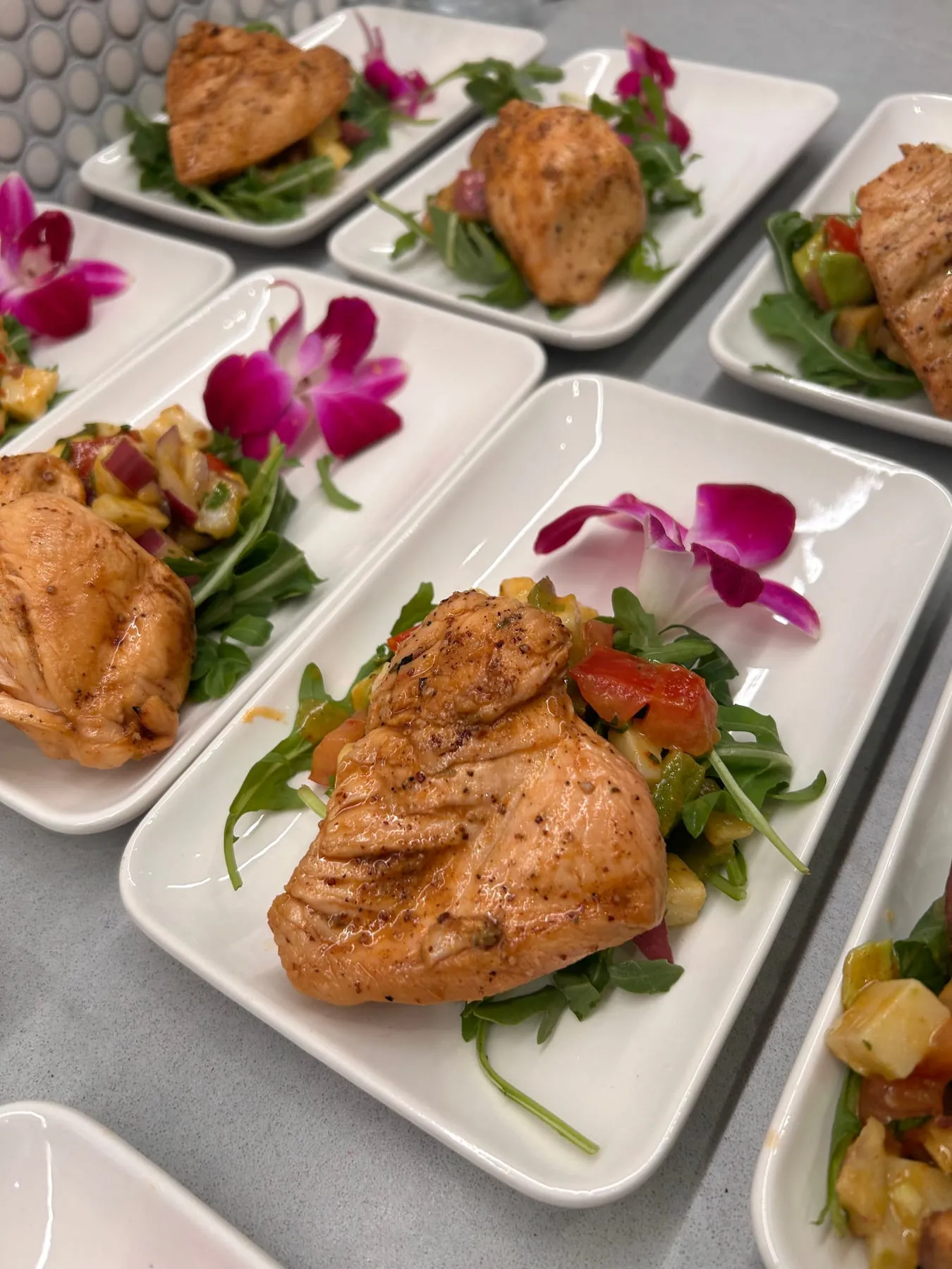 Plated chicken on arugula with pineapple salsa and an orchid garnish